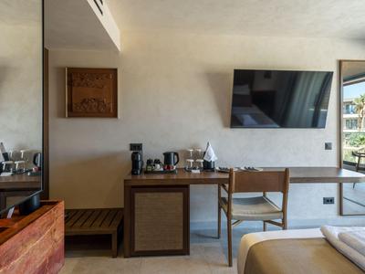 Habitación de hotel moderna con escritorio, silla, TV y vista al área exterior.