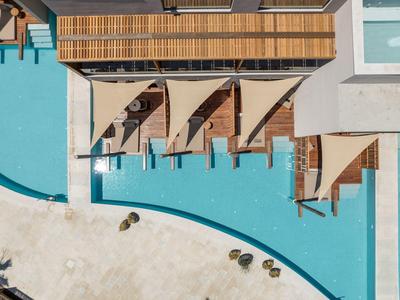 Vista general de tumbonas con toldos junto a una piscina azul en un área hotelera.