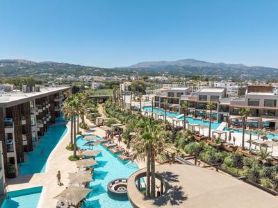 Complejo hotelero moderno con piscinas y palmeras en un paisaje soleado con montañas al fondo.