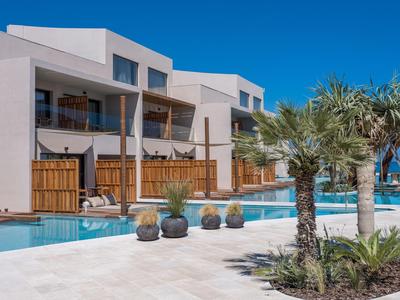Hotel moderno con piscina y palmeras bajo un cielo azul despejado.
