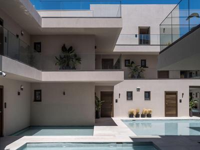 Patio moderno de hotel con piscina, paredes blancas y barandillas de vidrio bajo un cielo despejado.
