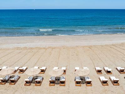 Pláž s lehátky a slunečníky uspořádaná v řadách před modrým mořem.