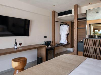 Moderní hotelový pokoj s TV, stolem, lahví vína a zavěšeným županem.