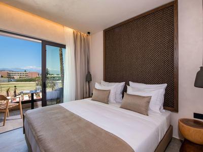 Habitación de hotel moderna con cama doble, balcón y vista a un paisaje verde.