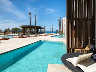 Venku bazén s výhledem na moře a zahradní nábytek pod modrou oblohou.