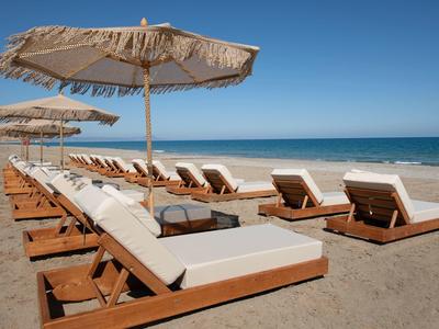 Dřevěná lehátka s polštáři pod slunečníky na pláži u moře.