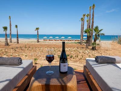 Two lounge chairs with towels beside a table with a wine bottle and glass on the beach.