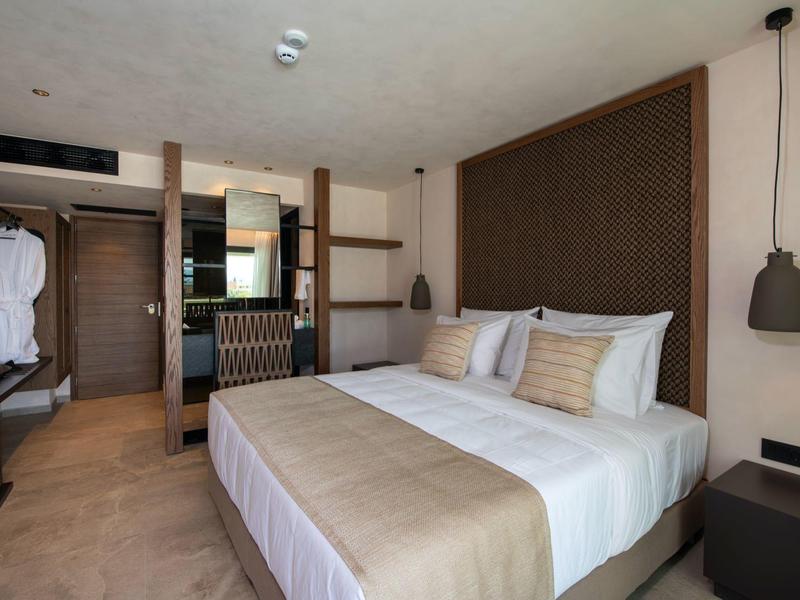 Elegantní hotelový pokoj s manželskou postelí, závěsnými lampami a béžovou výzdobou.