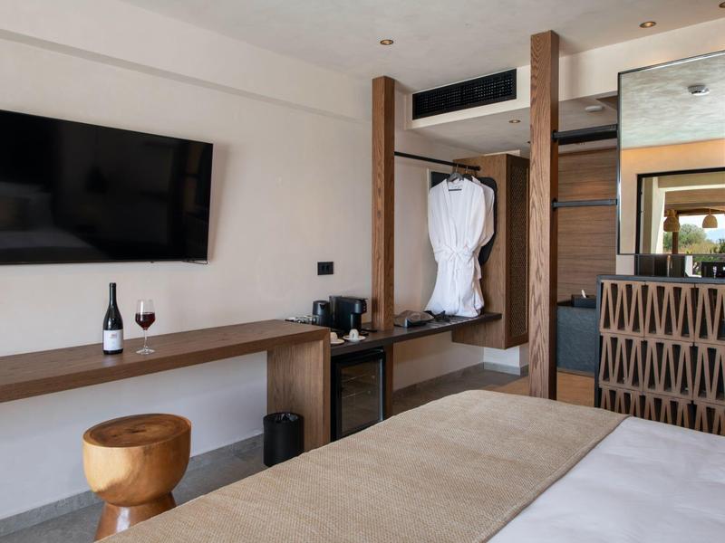 Moderní hotelový pokoj s TV, stolem, lahví vína a zavěšeným županem.
