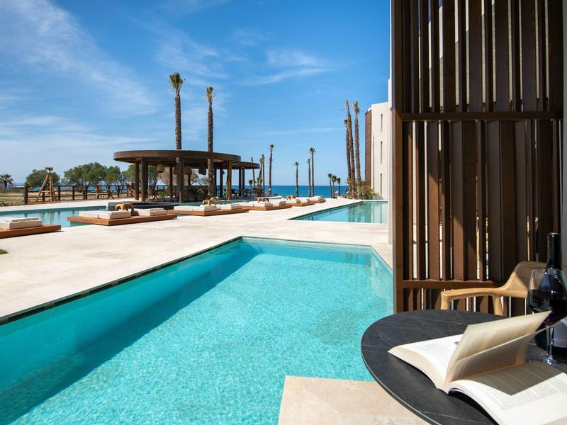 Venku bazén s výhledem na moře a zahradní nábytek pod modrou oblohou.