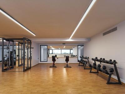 Heller Fitnessraum mit Holzfußboden, Gewichten und Trainingsgeräten.
