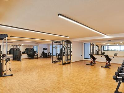 Großer Fitnessraum mit Holzfußboden, Hanteln und Trainingsgeräten in einem Hotel.