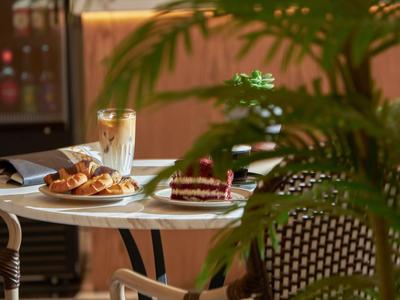 Kaffeetisch mit Croissants, Tortenstück und Latte Macchiato, umgeben von Pflanzen in einem Café.