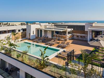Dachterrasse mit großem Pool, Liegestühlen und Blick auf das Meer bei klarem Himmel.