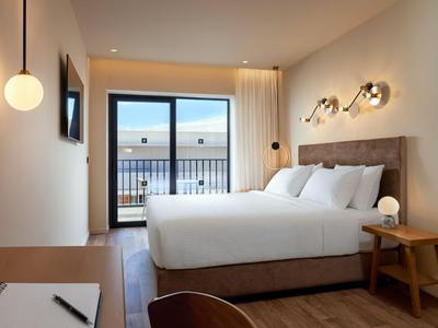 Modernes Hotelzimmer mit großem Bett, Holzmöbeln und Balkon mit Meerblick.