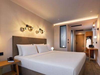 Modernes Hotelzimmer mit großem Bett, warmem Licht und schlichter Holz-Dekoration.
