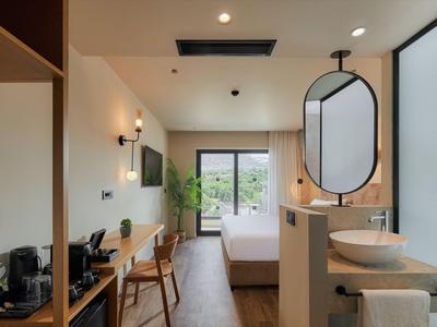 Modernes Hotelzimmer mit großem Fenster, Bett, Schreibtisch, Stuhl und Waschbecken.