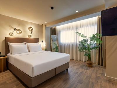 Modernes Hotelzimmer mit großem Bett, Holzfußboden und einer Pflanze neben dem Fenster.