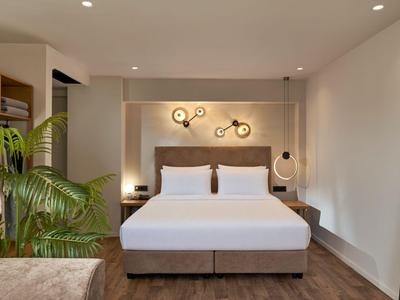 Modernes Hotelzimmer mit großem Bett, Pflanzen und schlichtem Dekor in neutralen Farben.
