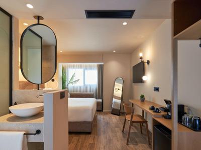 Modernes Hotelzimmer mit Doppelbett, Schreibtisch, Spiegel und offenen Badbereich.