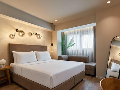 Modernes Hotelzimmer mit Doppelbett, Nachttisch, Spiegel und Fenster mit Vorhängen.