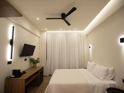 Modern eingerichtetes Hotelzimmer mit Doppelbett, Deckenventilator und Fernseher an der Wand.
