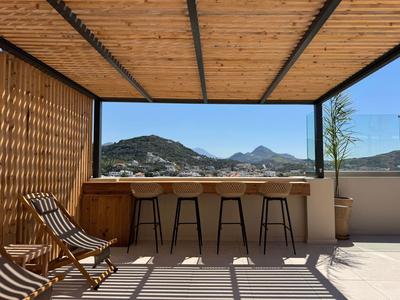 Dachterrasse mit Holzdach, Barhockern und Blick auf Berglandschaft bei klarem Himmel.
