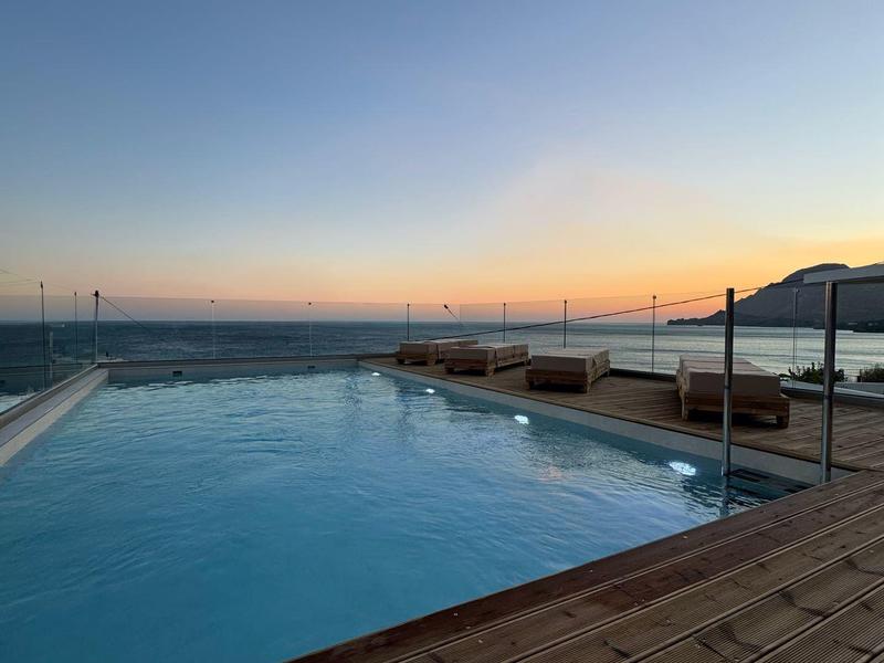 Ein ruhiger Pool mit Holzdeck bietet Blick auf das Meer bei Sonnenuntergang.