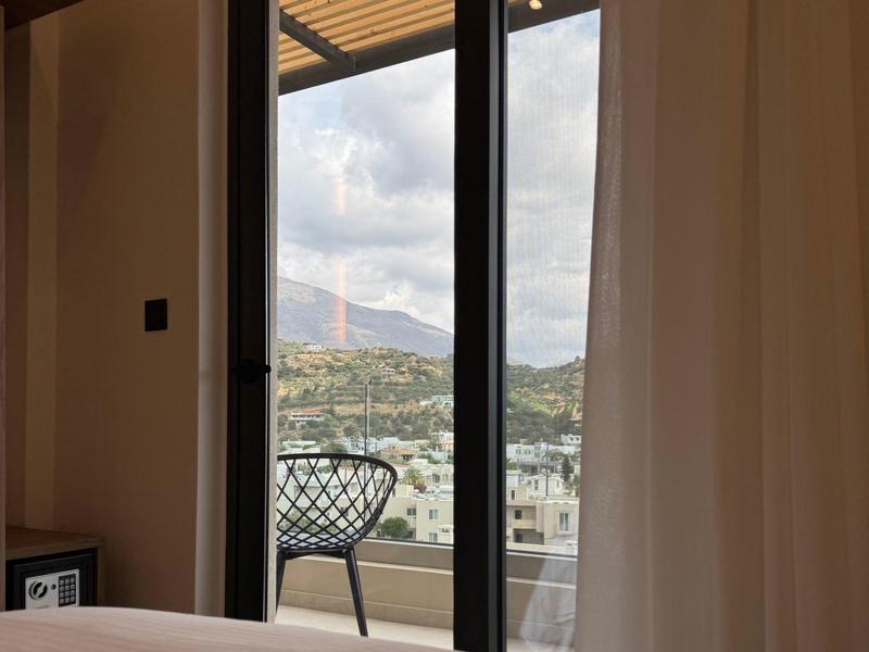 Blick aus einem Hotelzimmer mit Bett auf einen Balkon und eine Berglandschaft bei bewölktem Himmel.