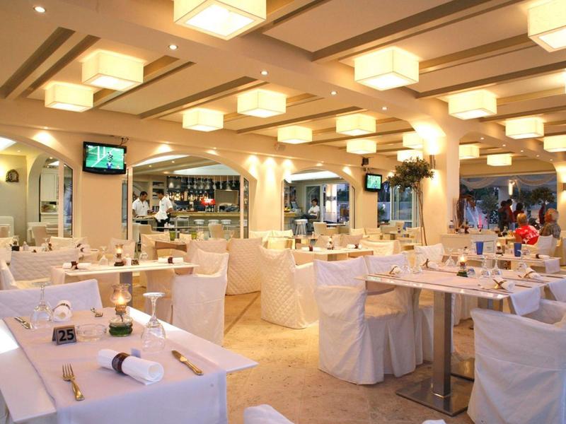 Heller Restaurantraum mit vielen weißen gedeckten Tischen und Deckenleuchten.