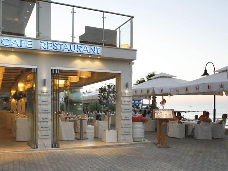 Ein helle Café mit Glasfront und Terrasse neben einem ruhigen Gewässer bei Sonnenuntergang.