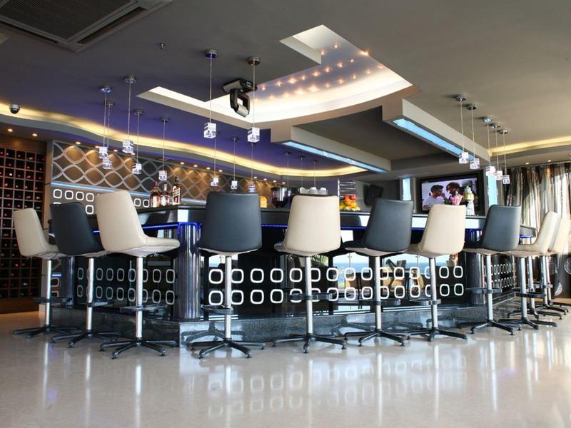 Moderner Barbereich mit hohen Hockern, geometrischem Tresen und dimmbarer Beleuchtung in hellem Raum.