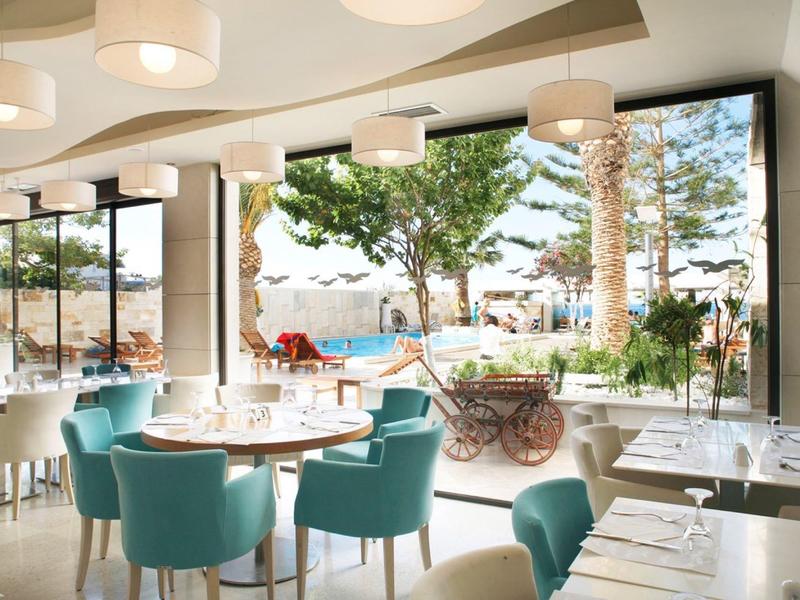 Modernes Restaurant mit blauen Stühlen, runden Tischen und großer Fensterfront zur Außenterrasse.