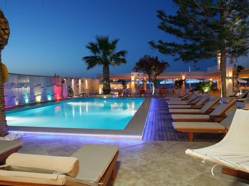 Moderner Außenpool bei Nacht mit Liegen, Palmen und indirekter Beleuchtung in warmem Ambiente.