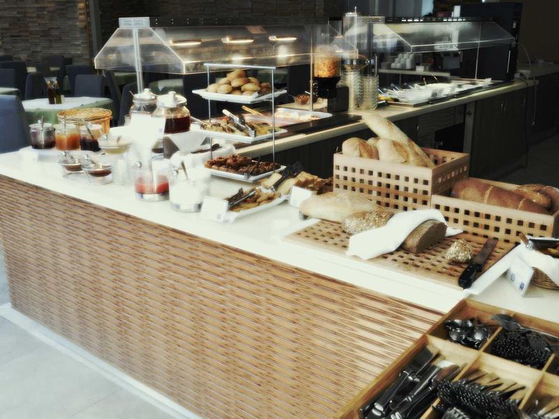 Buffet mit Brotauswahl, Gläsern, Besteck und diversen Speisen auf hellem Tisch mit Holzstruktur.