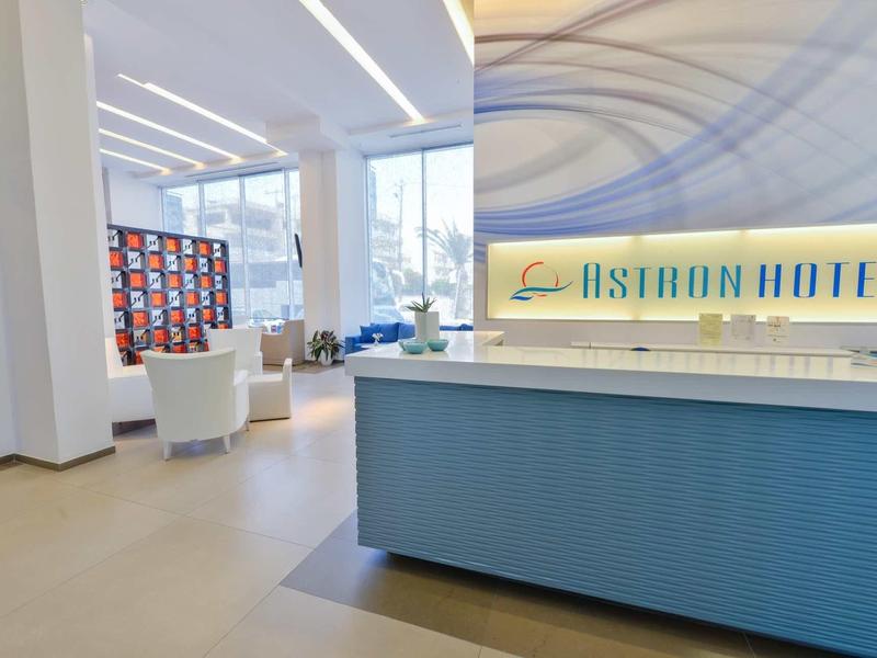 Moderner Hotel-Empfang mit blauer Rezeption, weißen Sesseln und großem Fensterlicht.