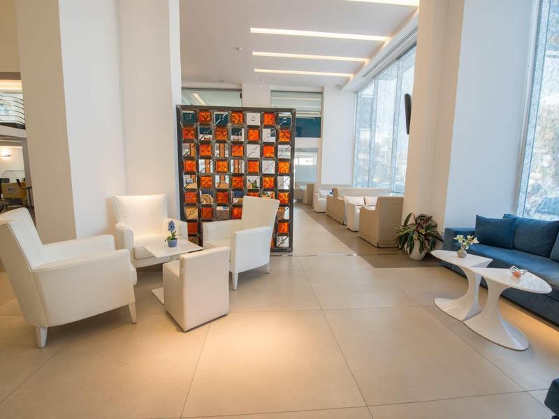 Moderner Wartebereich mit weißen Sesseln, blauem Sofa und farbenfrohem Raumteiler im hellen Raum.