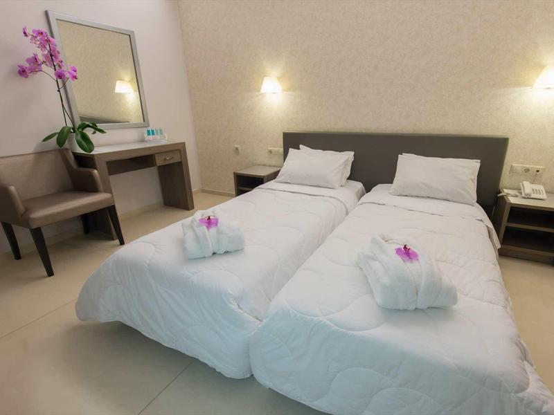 Zwei Einzelbetten mit weißen Bettdecken, Nachttischen, Stuhl und Kommode mit Spiegel und Blume.