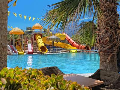 Waterpark met glijbanen en zwembad omgeven door palmbomen op een zonnige dag.