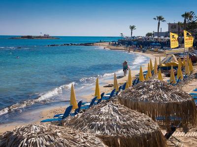 Strand met parasols en ligstoelen naast helder blauw zeewater op een zonnige dag.
