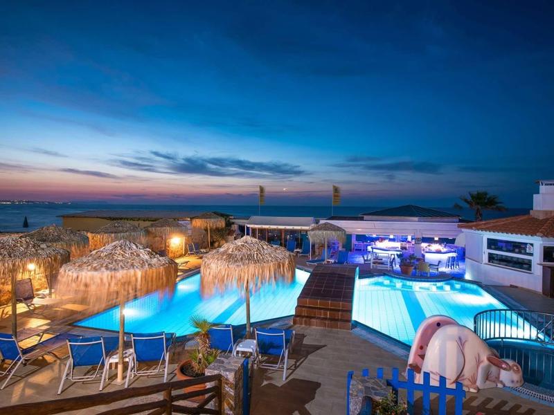 Osvětlená oblast bazénu s lehátky a slaměnými slunečníky poblíž pláže při západu slunce