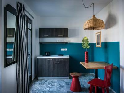 Piccola cucina con armadietti blu scuro, tavolo da pranzo, sedie colorate e decorazioni murali.