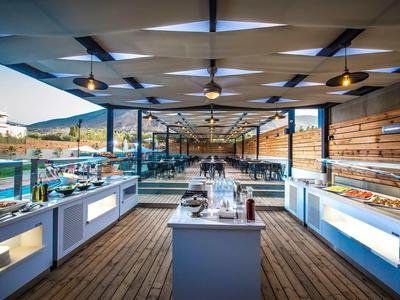 Buffet aperto con vari piatti e refrigeratori su una terrazza in legno con vista mare.