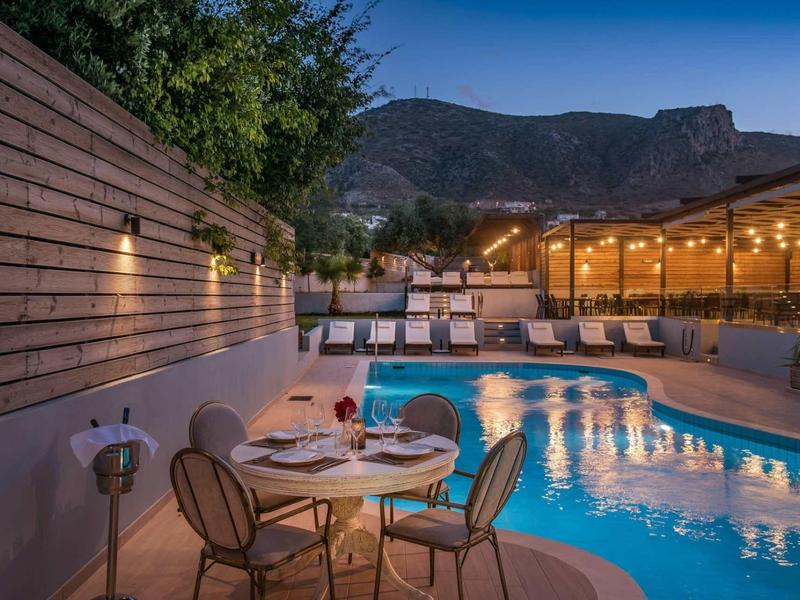 Area piscina dell'hotel illuminata con sedute e veranda al crepuscolo.