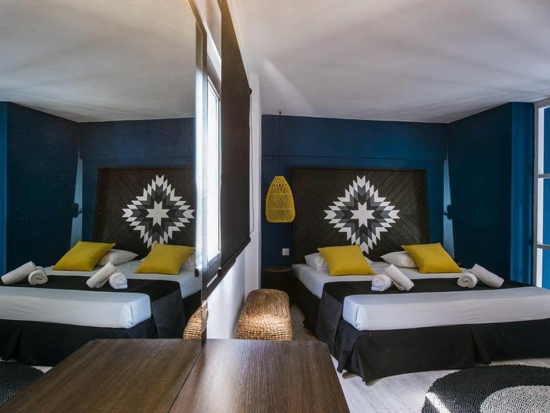 Camera d'hotel con due letti, pareti blu-verdi e decorazioni sulle testate dei letti.