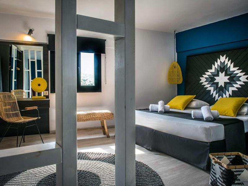 Camera d'hotel moderna con parete blu, letto matrimoniale, sedia e scrivania con specchio.