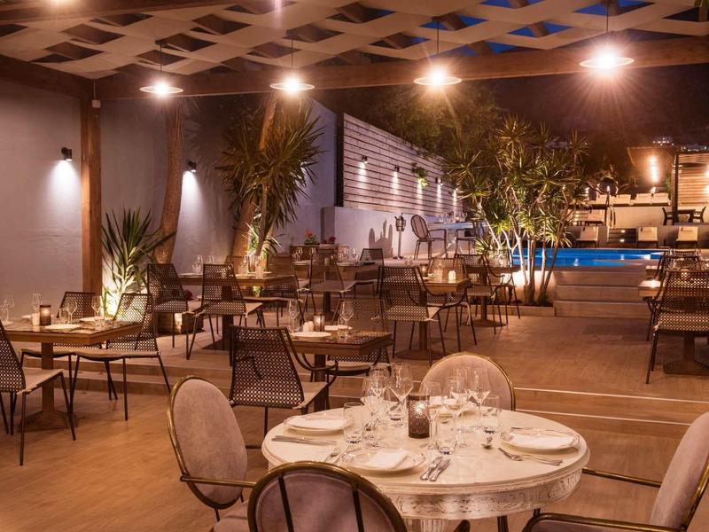 Ristorante all'aperto elegante con tavoli apparecchiati sotto luce calda e piscina sullo sfondo.