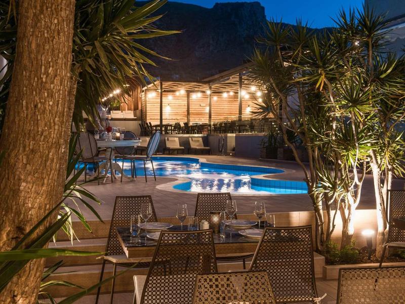 Terrazza serale con posti a sedere e piscina illuminata davanti a un ristorante.