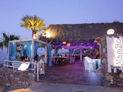 Un bar sulla spiaggia con tetto di paglia, illuminazione decorativa e palme al tramonto.