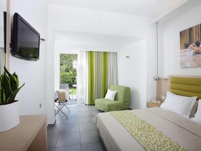 Camera d'hotel luminosa con letto matrimoniale, poltrona verde e TV a muro.